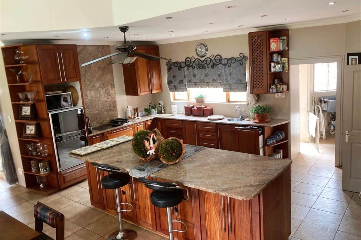 Spacious kitchen featuring wooden cabinetry, granite countertops, a central island with breakfast bar seating, and integrated oven and hob.