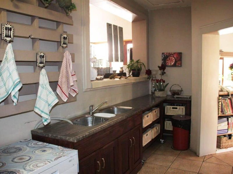 A functional scullery area featuring a double sink, laminate countertops, and built-in wooden cabinetry with open shelving for storage.