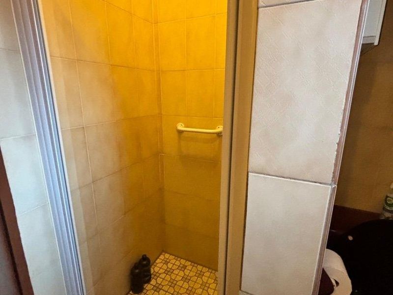 A compact shower stall featuring tiled walls, a grab rail, and a glass enclosure, currently showing signs of wear and dated finishes.