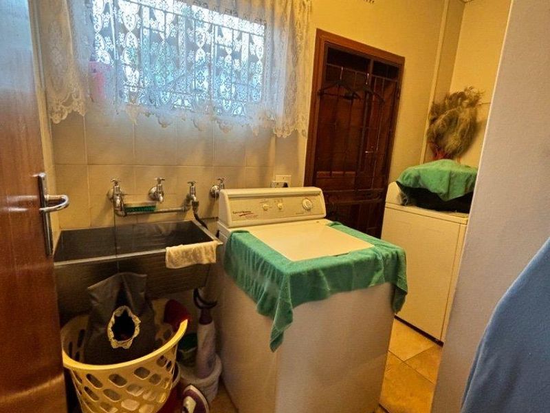 A functional laundry room featuring a stainless steel sink, wall-mounted taps, and tiled splashback, providing a practical space for household utility tasks.