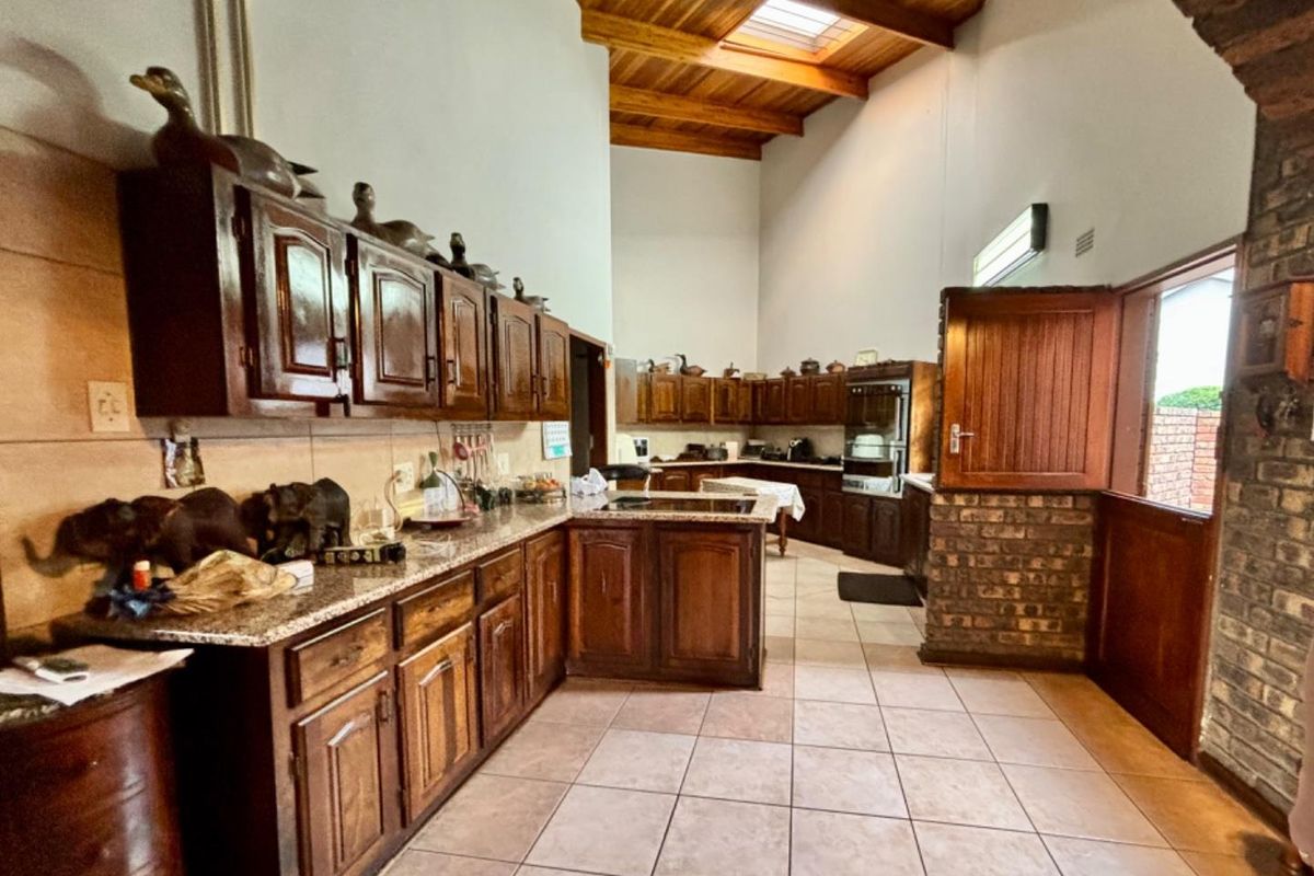 Spacious kitchen featuring dark wood cabinetry, granite countertops, high vaulted timber ceilings with a skylight, and a unique brick feature wall.