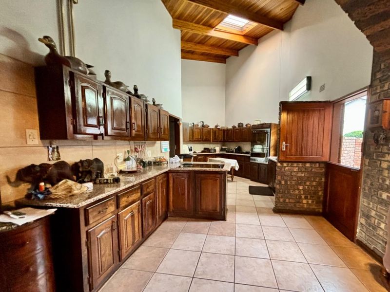 Spacious kitchen featuring dark wood cabinetry, granite countertops, high vaulted timber ceilings with a skylight, and a unique brick feature wall.