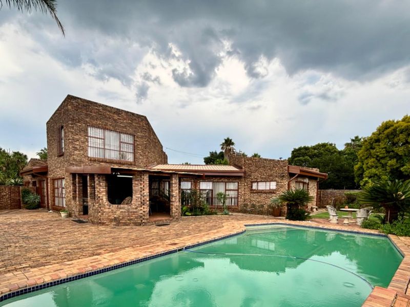 Rear view of a face brick house featuring a swimming pool, paved patio area, and covered outdoor space under a metal roof.