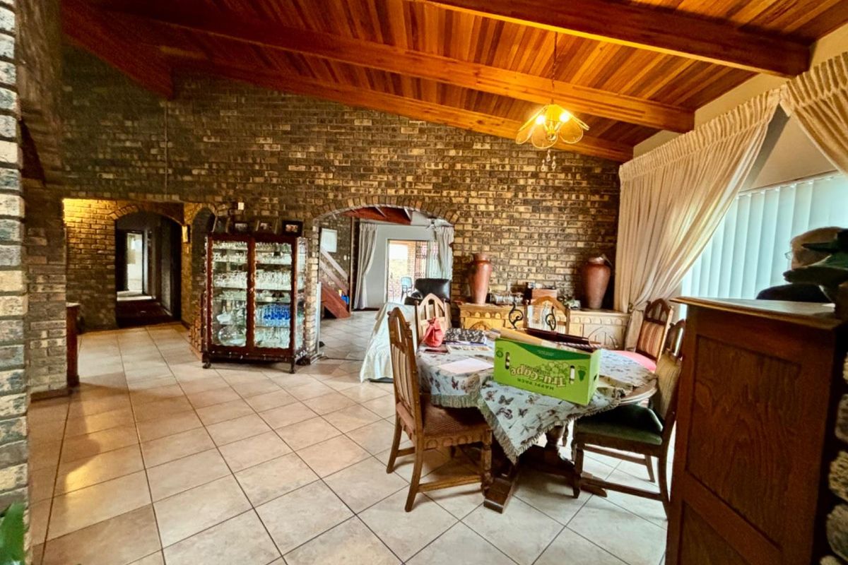 Spacious living area featuring rustic face brick walls, high exposed timber beam ceilings, and neutral ceramic floor tiles with arched architectural transitions.