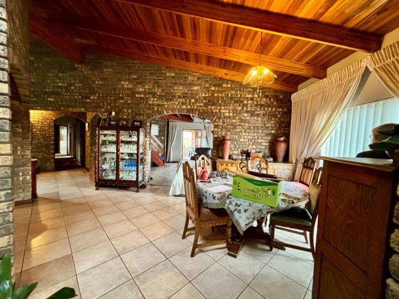 Spacious living area featuring rustic face brick walls, high exposed timber beam ceilings, and neutral ceramic floor tiles with arched architectural transitions.