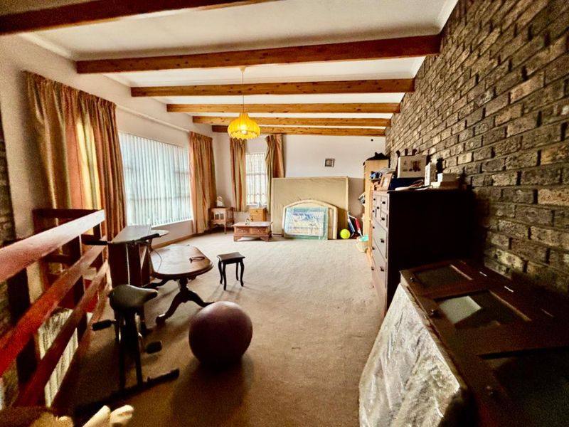 Spacious living area featuring exposed timber ceiling beams and a prominent brick feature wall, offering a rustic aesthetic with significant potential for modernization.