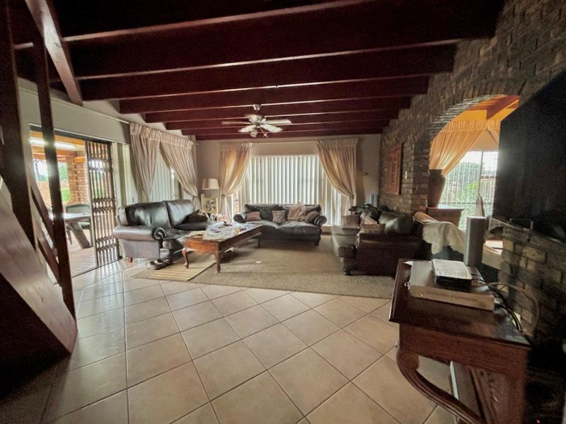 Spacious living room featuring exposed timber ceiling beams, a rustic brick feature wall, ceramic floor tiling, and direct access to an outdoor patio area.