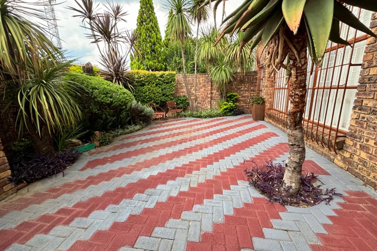 A well-maintained rear courtyard featuring patterned brick paving, established garden beds, and secure brick boundary walls.