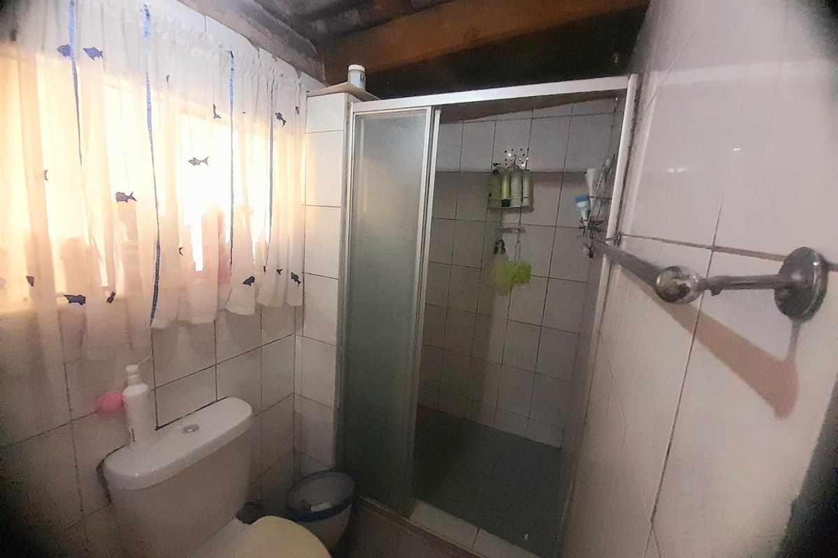 A compact bathroom featuring a tiled shower enclosure, standard toilet, and exposed ceiling beams, requiring modernization to improve functionality and aesthetic appeal.