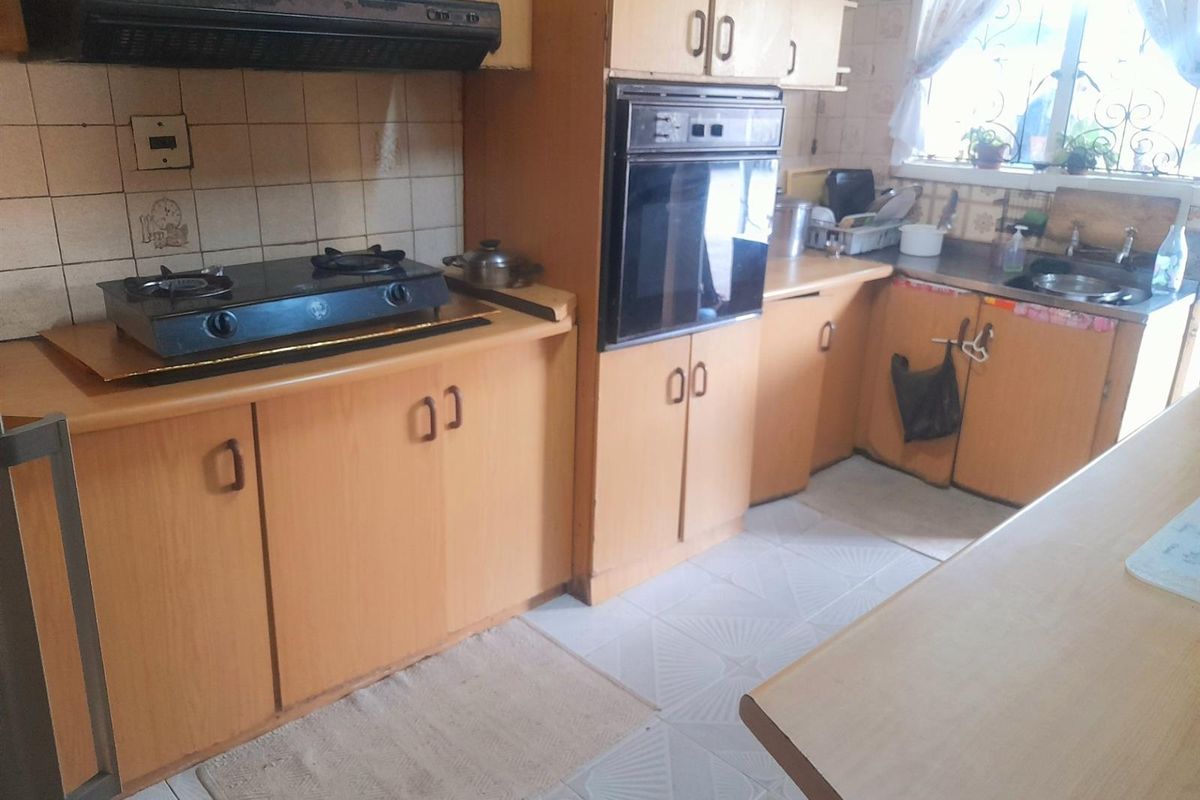 A dated kitchen featuring wood-look cabinetry, built-in oven, gas hob, extractor fan, and tiled flooring with a functional layout.