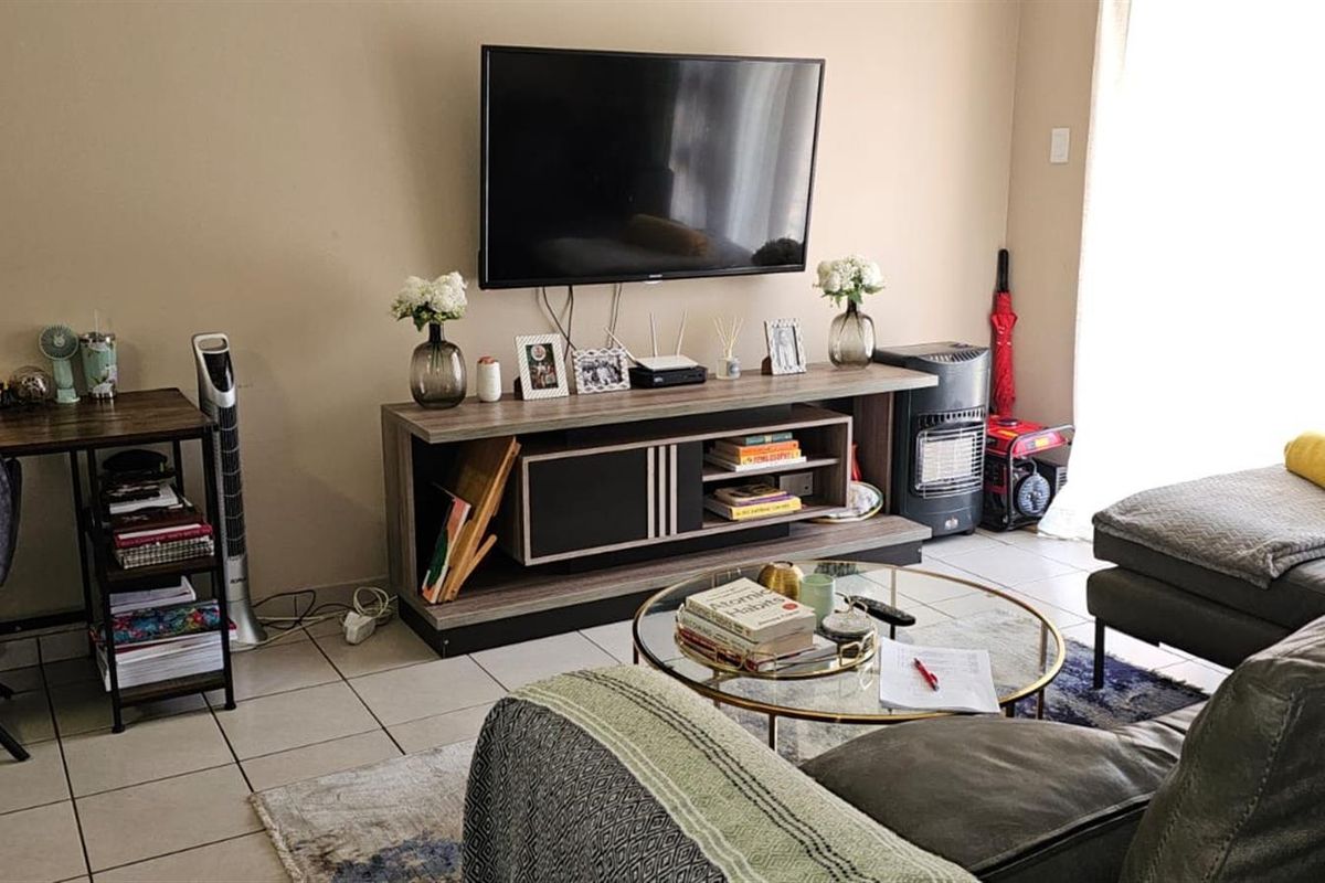 A comfortable living room featuring tiled flooring and a wall-mounted television setup, providing a functional and inviting space for relaxation.