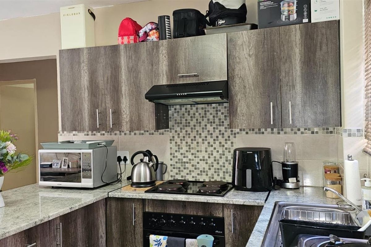 A functional kitchen featuring wood-grain cabinetry, granite countertops, a mosaic tile backsplash, and a built-in hob with an extractor fan.