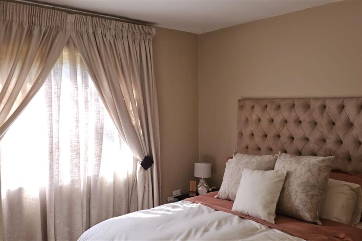 A cozy bedroom featuring neutral wall tones and natural light filtering through window curtains.