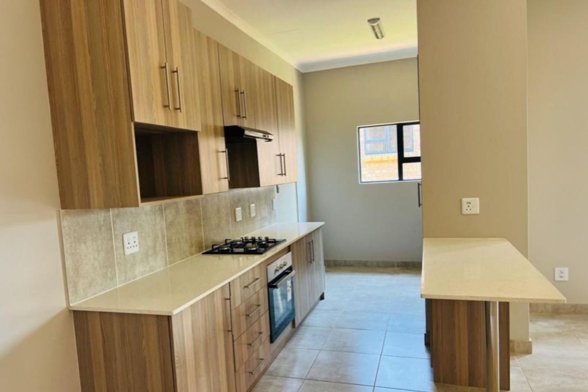 Modern kitchen featuring wood-finish cabinetry, stone countertops, a built-in gas hob, oven, and an integrated breakfast bar.