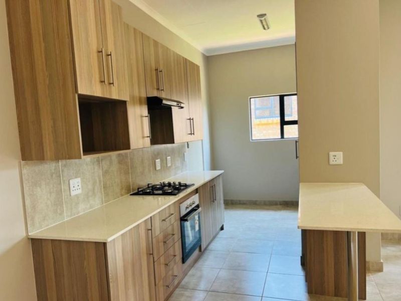 Modern kitchen featuring wood-finish cabinetry, stone countertops, a built-in gas hob, oven, and an integrated breakfast bar.