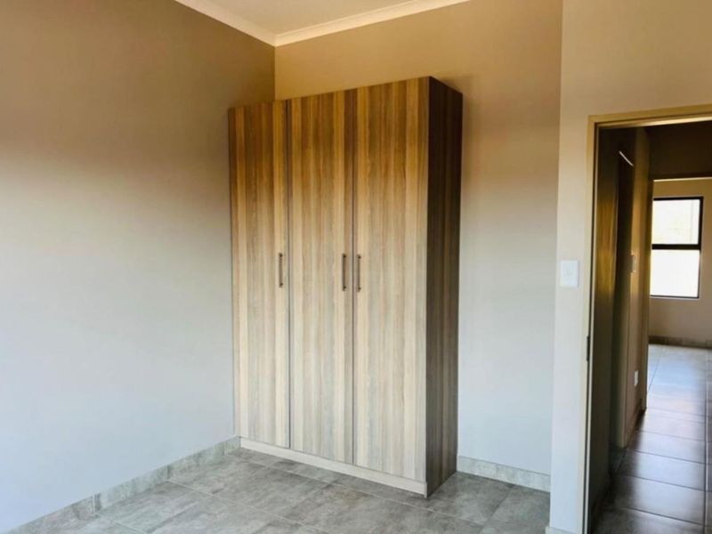 A bedroom featuring built-in wooden cabinetry and tiled flooring, with a view leading into an adjacent hallway.