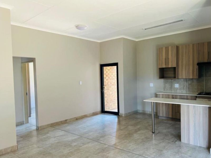 An open-plan living and kitchen area featuring tiled flooring, wood-look cabinetry, and a breakfast bar, with direct access to an exterior space.