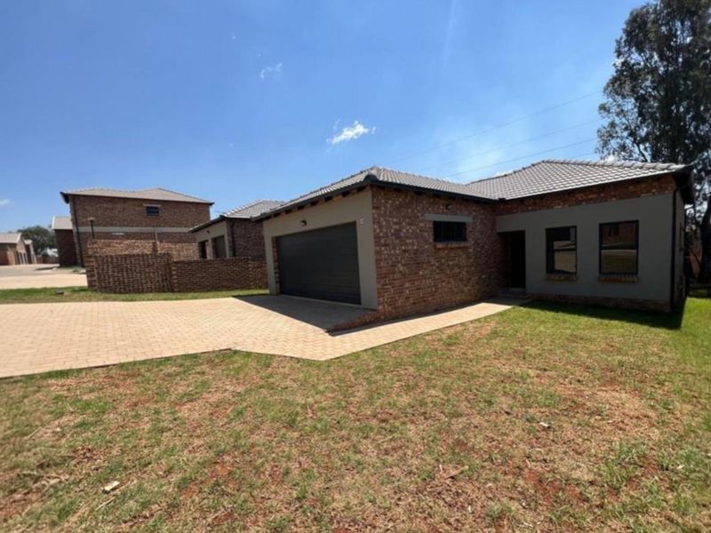 A modern townhouse exterior featuring a brick facade, tiled roof, paved driveway, and an integrated garage, set within a well-maintained residential complex.