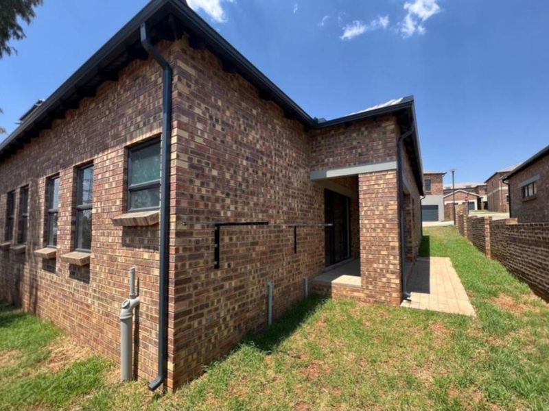 A view of the rear exterior of the townhouse, featuring face-brick walls, black guttering, and a paved patio area leading to the garden.