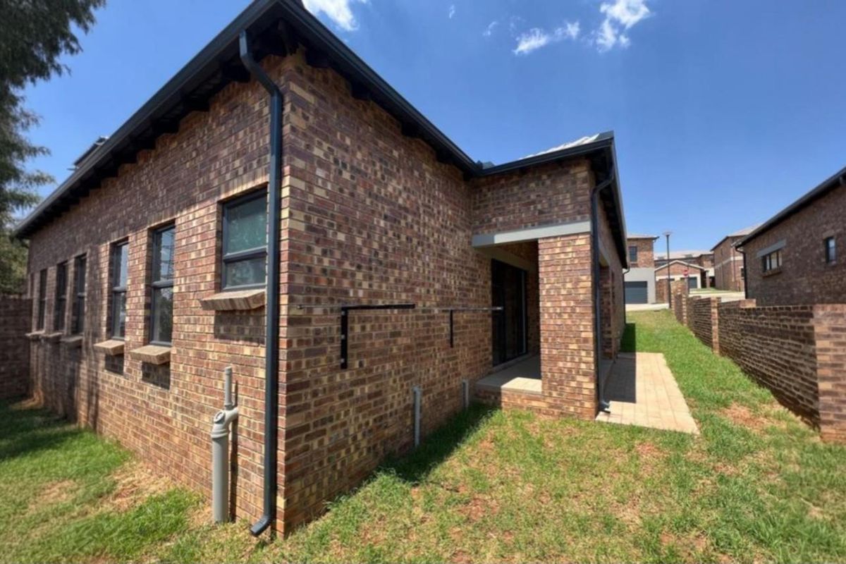 A view of the rear exterior of the townhouse, featuring face-brick walls, black guttering, and a paved patio area leading to the garden.