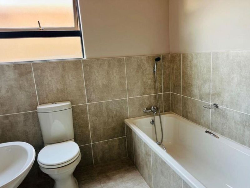 A functional bathroom featuring a built-in bathtub with a handheld shower attachment, a standard toilet, and neutral wall tiling.
