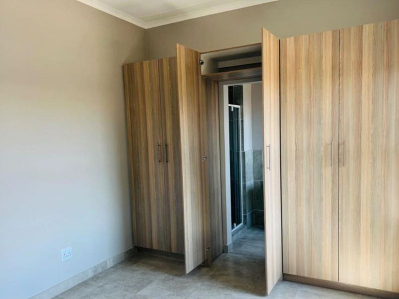 A bedroom featuring built-in wooden cupboards and direct access to an en-suite bathroom with tiled flooring.