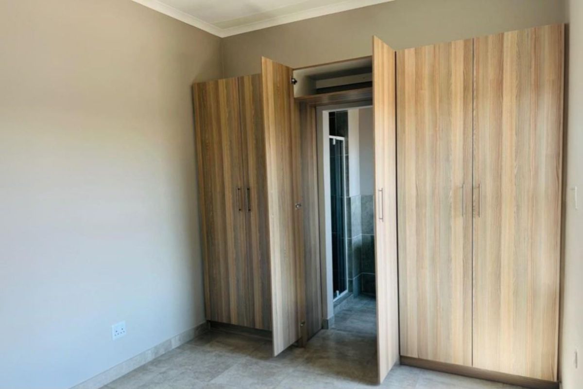 A bedroom featuring built-in wooden cupboards and direct access to an en-suite bathroom with tiled flooring.