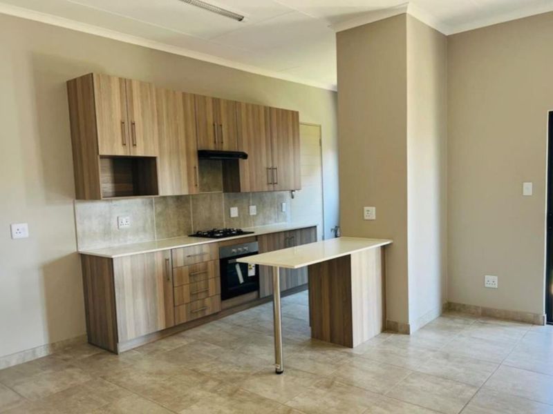 Modern open-plan kitchen featuring wood-grain cabinetry, built-in oven, gas hob, extractor fan, and a breakfast bar, with direct access to the outdoor area.