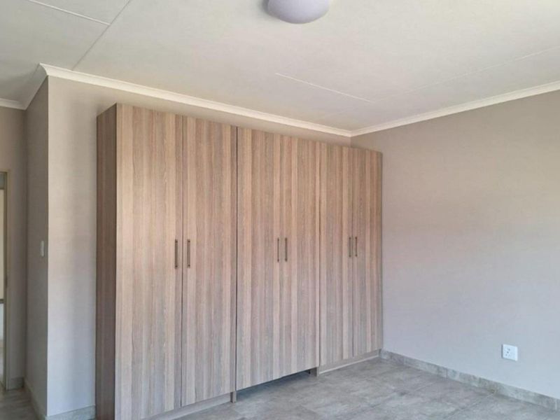 A clean, neutral bedroom featuring modern wood-finish built-in cupboards and durable tiled flooring.