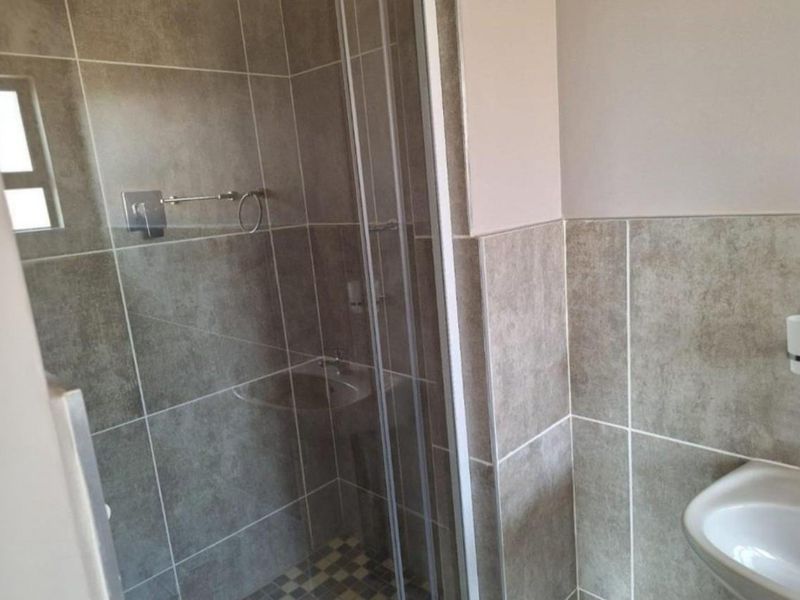 A clean, modern bathroom featuring a glass shower enclosure, wall-mounted basin, and neutral-toned wall and floor tiling.