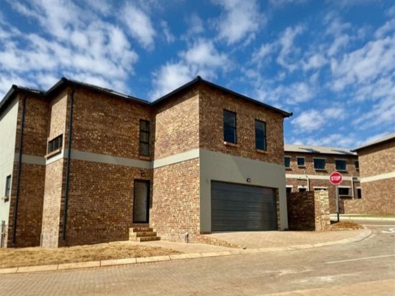 Front elevation of a modern face brick townhouse featuring a double garage and paved driveway in a residential estate setting.
