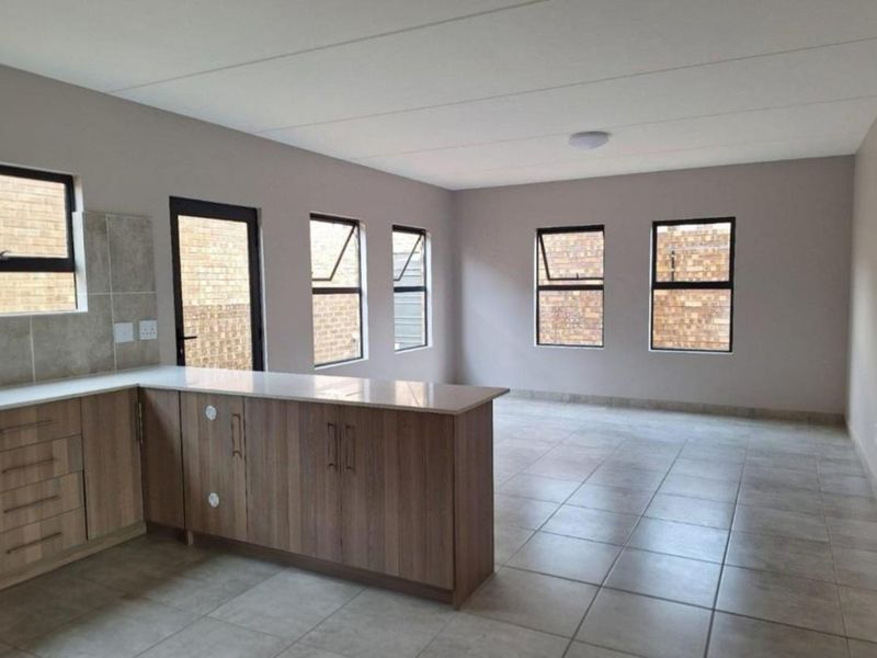 Spacious open-plan living area featuring modern kitchen cabinetry with stone countertops, neutral tiled flooring, and large windows providing ample natural light.