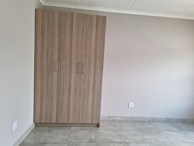 A clean, empty bedroom featuring neutral wall tones, tiled flooring, and a modern built-in wooden wardrobe.