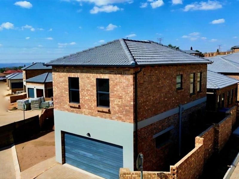 Aerial view of a modern double-story townhouse featuring a face brick exterior, tiled roof, and an integrated garage within a secure residential complex.