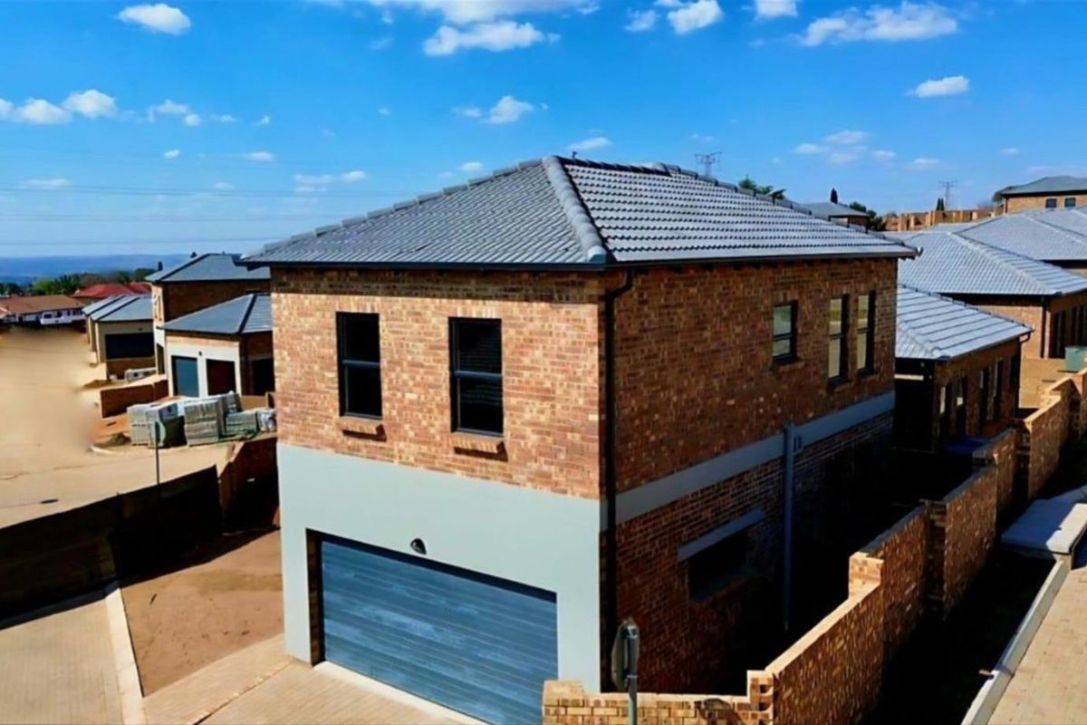 Aerial view of a modern double-story townhouse featuring a face brick exterior, tiled roof, and an integrated garage within a secure residential complex.