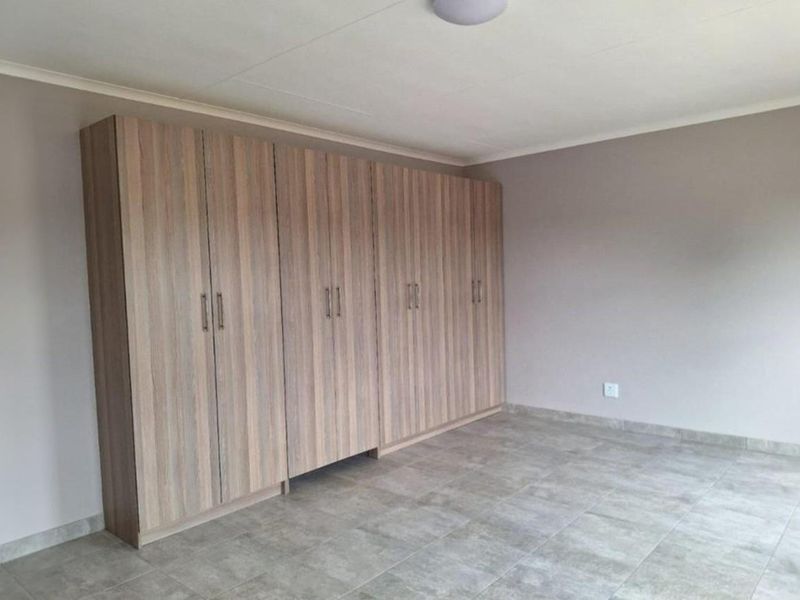 A spacious, empty bedroom featuring neutral wall tones, tiled flooring, and extensive built-in wooden cupboards for ample storage.