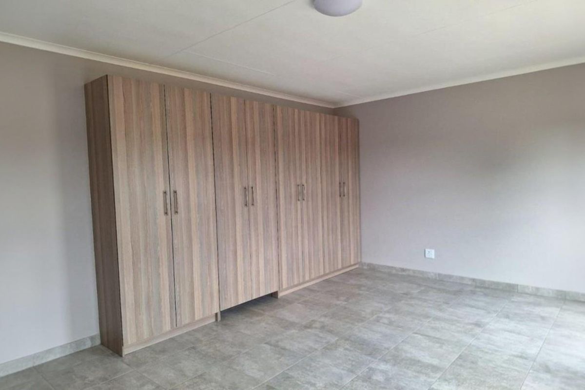 A spacious, empty bedroom featuring neutral wall tones, tiled flooring, and extensive built-in wooden cupboards for ample storage.
