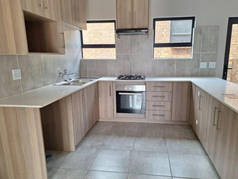Modern kitchen featuring light wood-grain cabinetry, stone countertops, built-in oven, gas hob, and extractor fan with neutral tiled finishes.