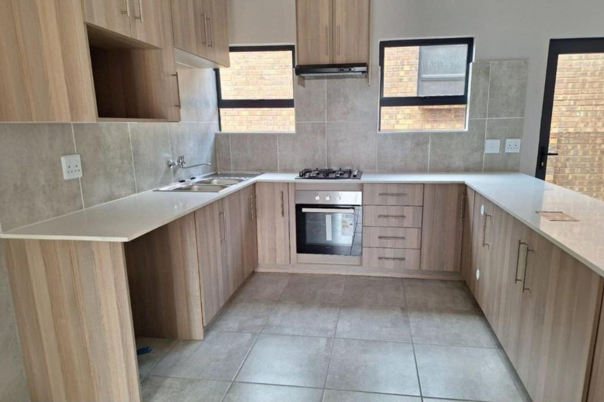 Modern kitchen featuring light wood-grain cabinetry, stone countertops, built-in oven, gas hob, and extractor fan with neutral tiled finishes.