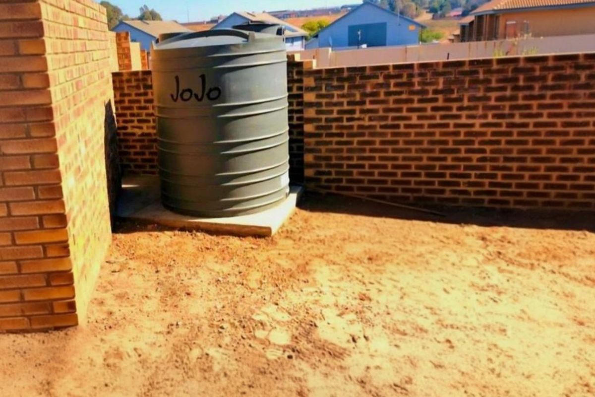 Rear exterior area featuring a water storage tank and brick boundary walls, with an unlandscaped ground surface ready for garden development.