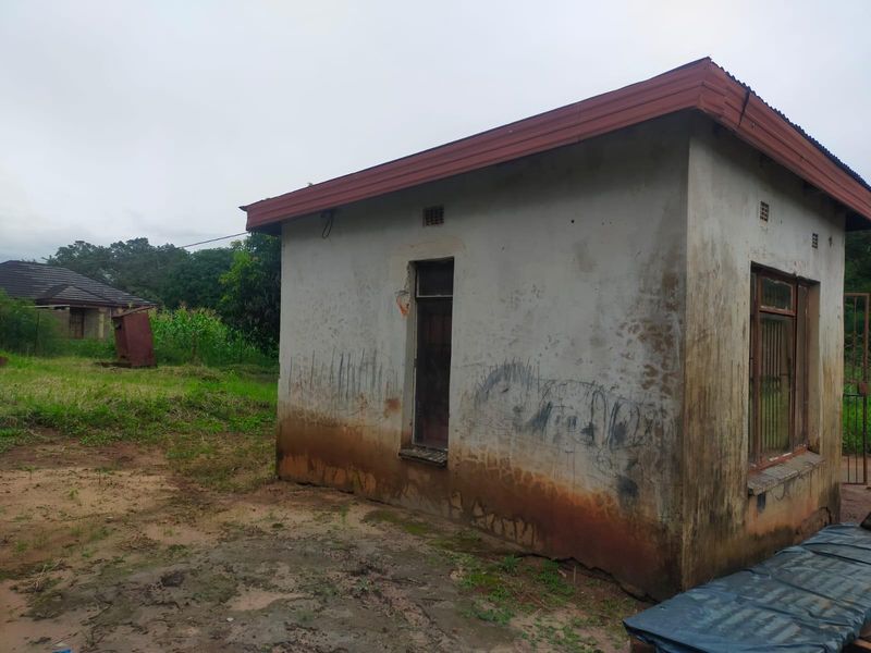 Exterior view of a small, weathered outbuilding featuring a corrugated metal roof and steel window frames with security bars.