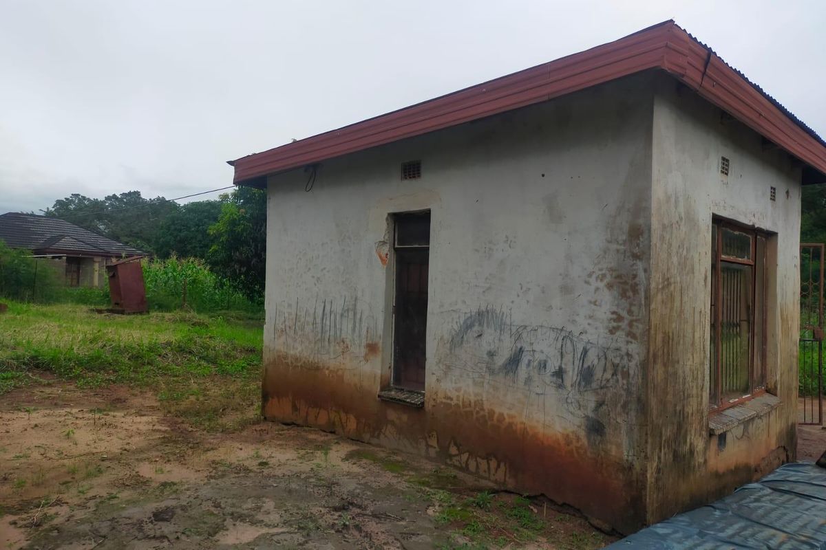 Exterior view of a small, weathered outbuilding featuring a corrugated metal roof and steel window frames with security bars.