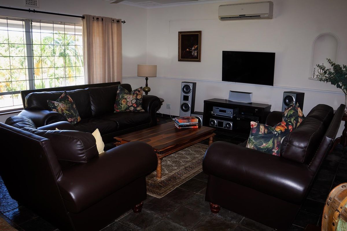A comfortable living room featuring tiled flooring, a wall-mounted air conditioning unit, and a large window with security bars.