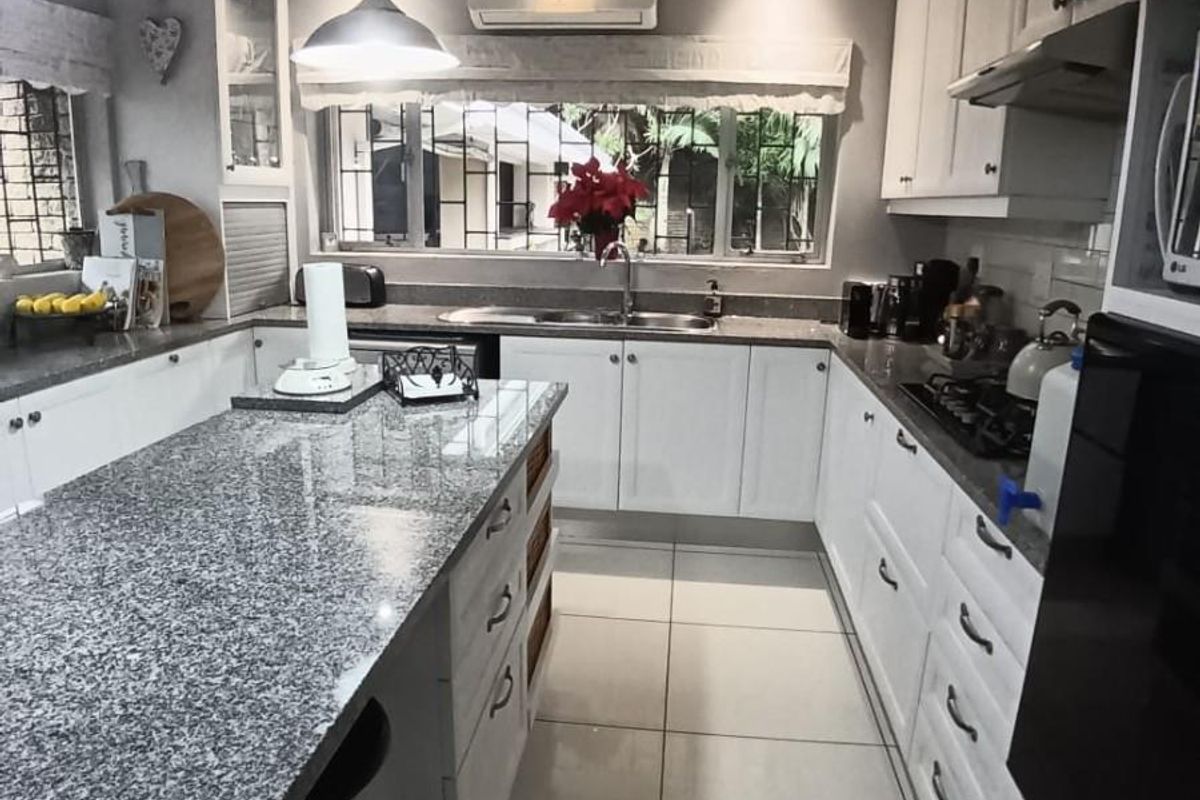 Modern kitchen featuring white cabinetry, granite countertops, a central island, tiled flooring, and integrated appliances including a gas hob and extractor fan.