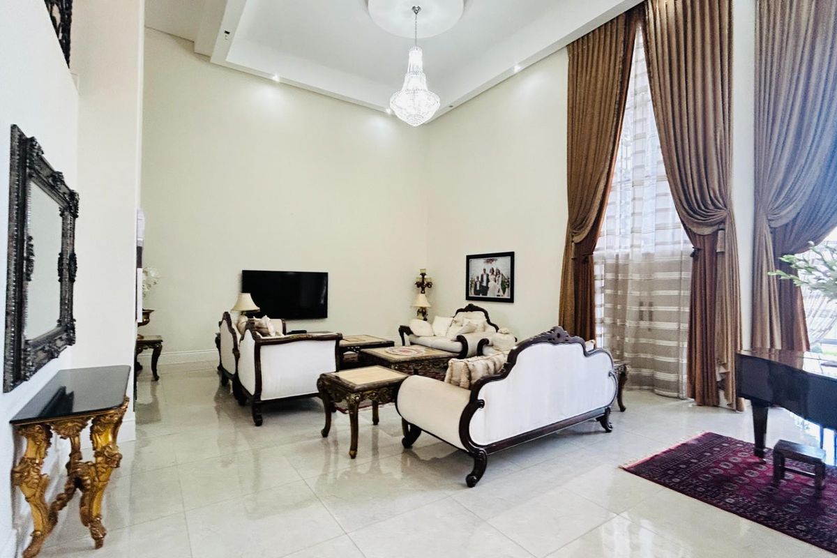 Spacious living room featuring high ceilings, large windows with floor-to-ceiling curtains, polished tile flooring, and a decorative chandelier.