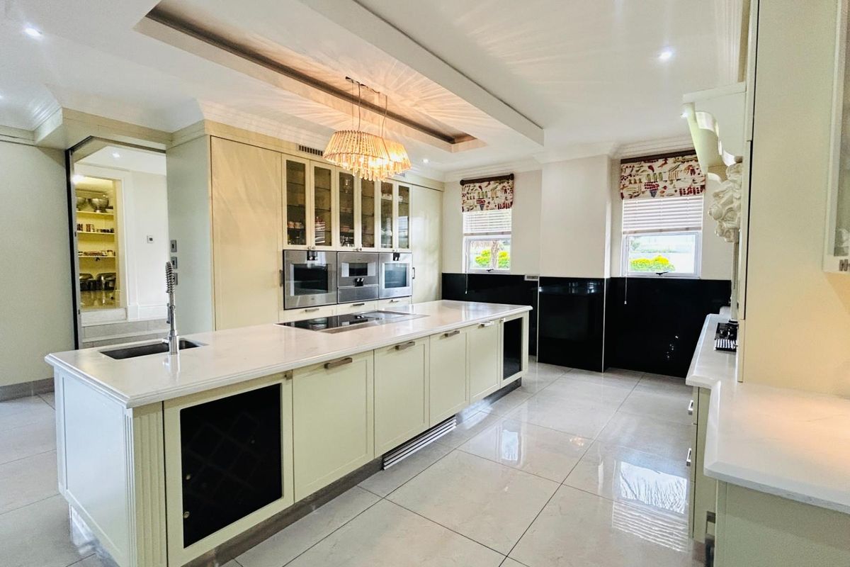 Spacious modern kitchen featuring a large central island with stone countertops, integrated appliances, built-in ovens, and high-gloss cabinetry with a walk-in pantry.