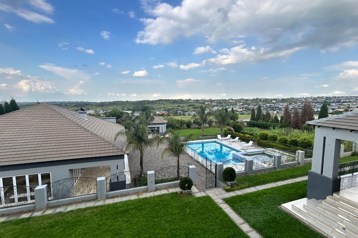 Elevated aerial view of a residential property featuring a swimming pool, landscaped garden, and expansive views of the surrounding landscape.