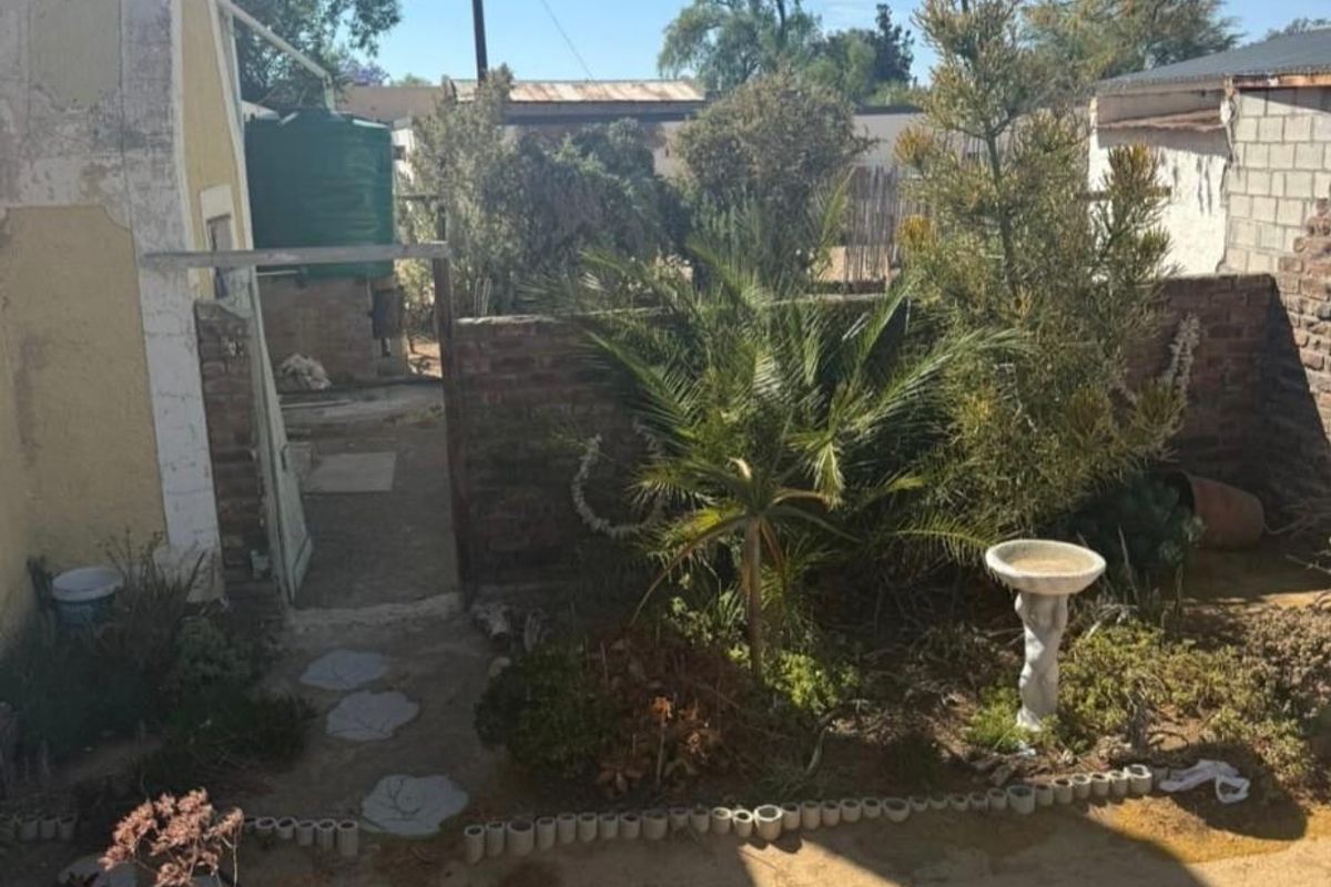 Rear garden area featuring a brick boundary wall, water tank, and paved pathway, showing signs of significant wear and maintenance requirements.