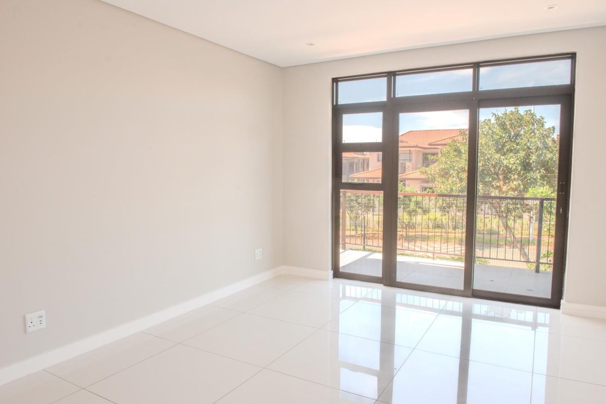 A bright, empty bedroom featuring polished porcelain floor tiles, neutral walls, and large sliding glass doors opening onto a private balcony.