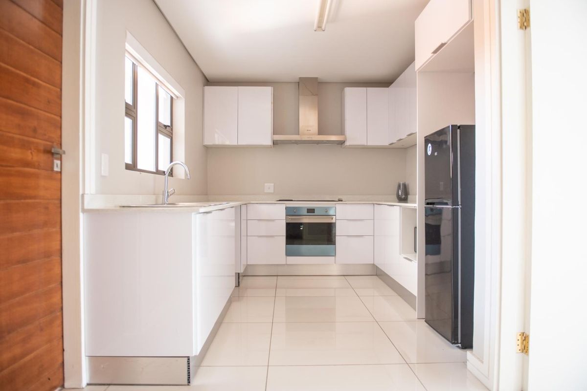 Modern kitchen featuring white high-gloss cabinetry, integrated oven, stainless steel extractor fan, and polished floor tiles.